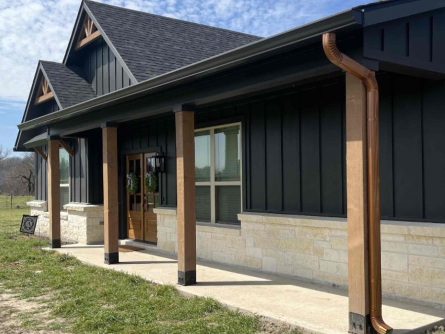 Black seamless gutters on a modern home exterior with copper-toned downspouts.