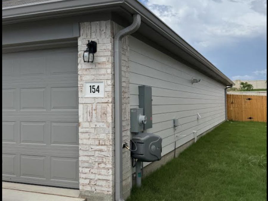 Garage side wall with white downspout and gutter installation.